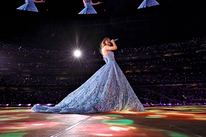 Taylor swift on stage during her Eras tour, wearing a blue ball gown and singing
