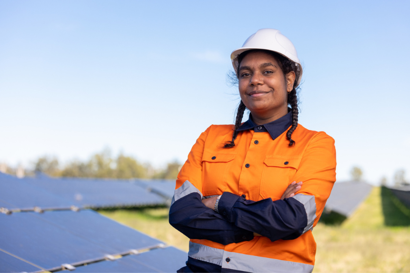 Photo of an Indigenous female engineer. She is posing in front of solar panels. Her pose is very powerful and confident. 